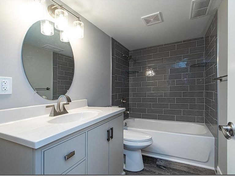 Remodeled bathroom by Avexa with gray subway tile tub surround and round mirror